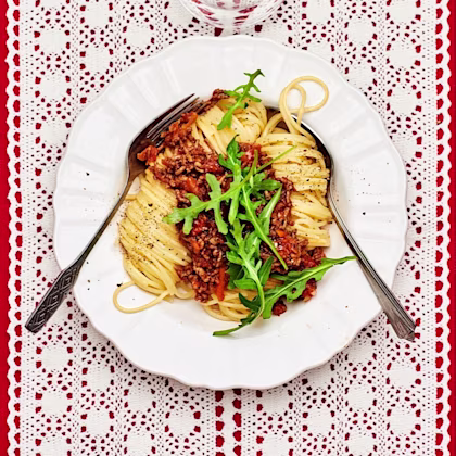 Spaghetti bolognese med ruccola på toppen och ett glas vatten bredvid
