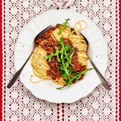 Spaghetti bolognese med ruccola på toppen och ett glas vatten bredvid