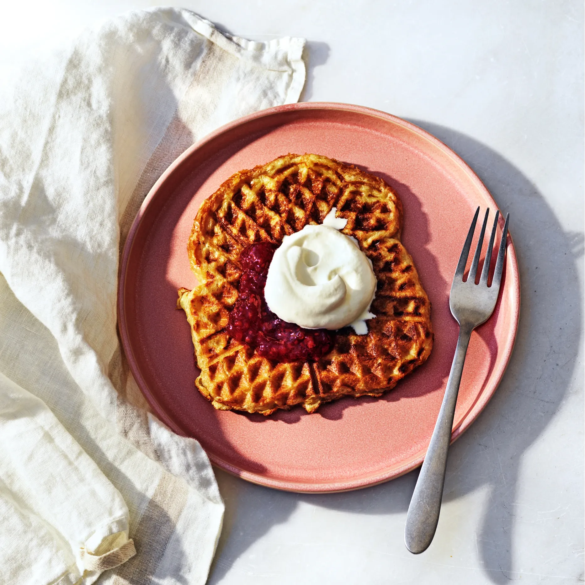 Rosa tallrik med en våffla toppad med sylt och grädde. 