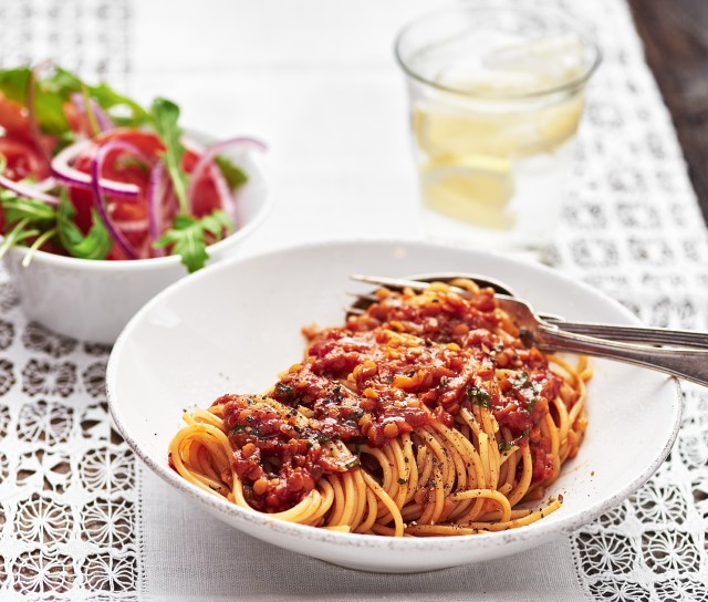 Spagetti med linsbolognese, sallad i en skål bredvid och ett glas citronvatten