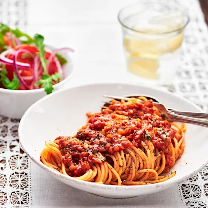 Spagetti med linsbolognese, sallad i en skål bredvid och ett glas citronvatten