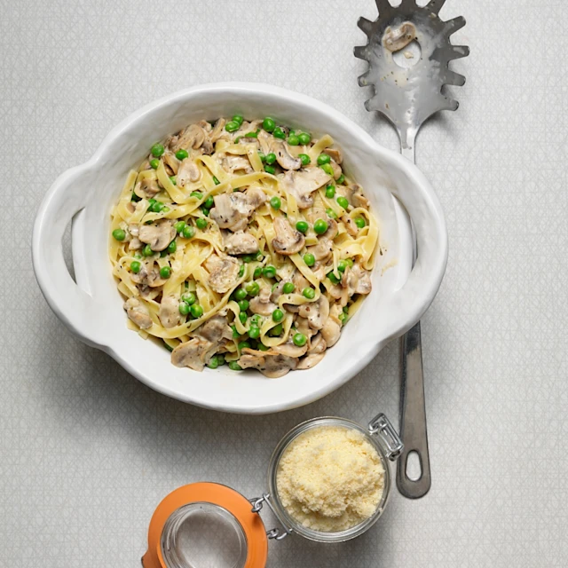 Tagliatelle med champinjoner, vitlök och ärter, parmesan i en burk bredvid