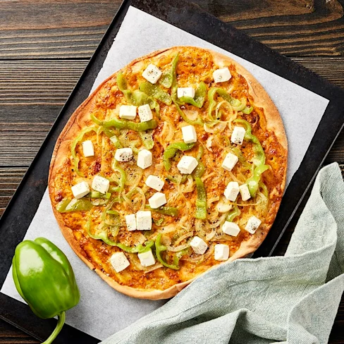 Pizza med grön paprika, lökar och fetaost på en bakplåt, med en grön paprika bredvid och en duk i hörnet.