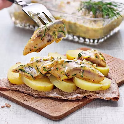 Potatisskivor och dillkryddad sill med sås läggs på ett knäckebröd på en skärbräda.
