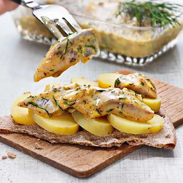 Potatisskivor och dillkryddad sill med sås läggs på ett knäckebröd på en skärbräda.