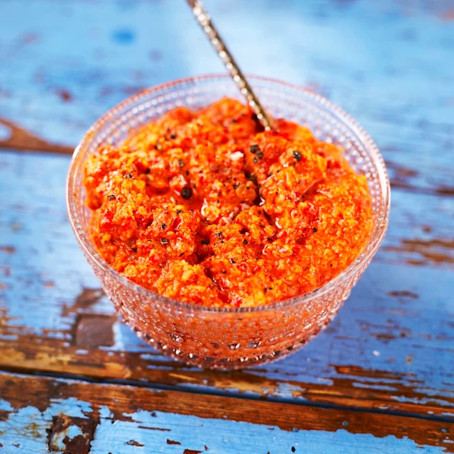 En härlig orange sås/röra i en transparent skål som står på ett blått, slitet bord.