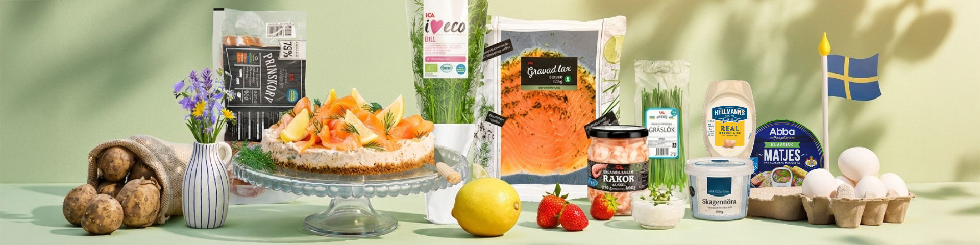 Midsommarbord med tårta toppad med jordgubbar, färsk dill, förpackning “Gravad lax”, “ICA Eco Dill”, burkar med “Räkor” och “Skagenröra”, majonnäs “Hellmann’s Real”, “Abba Matjes”, ägg och potatis. Klicka för att handla.