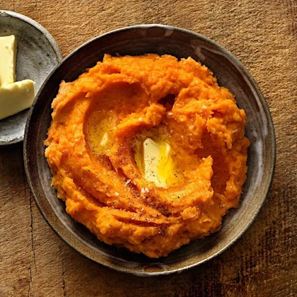 En skål med potatismos av sötpotatis. I mitten ligger en klick smör.