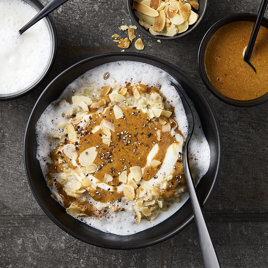 Djup tallrik med gröt. Toppad med skummad mjölk, mandelmassa och mandelflarn. 