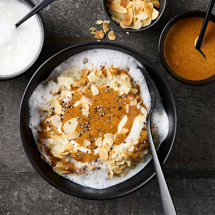 Djup tallrik med gröt. Toppad med skummad mjölk, mandelmassa och mandelflarn.