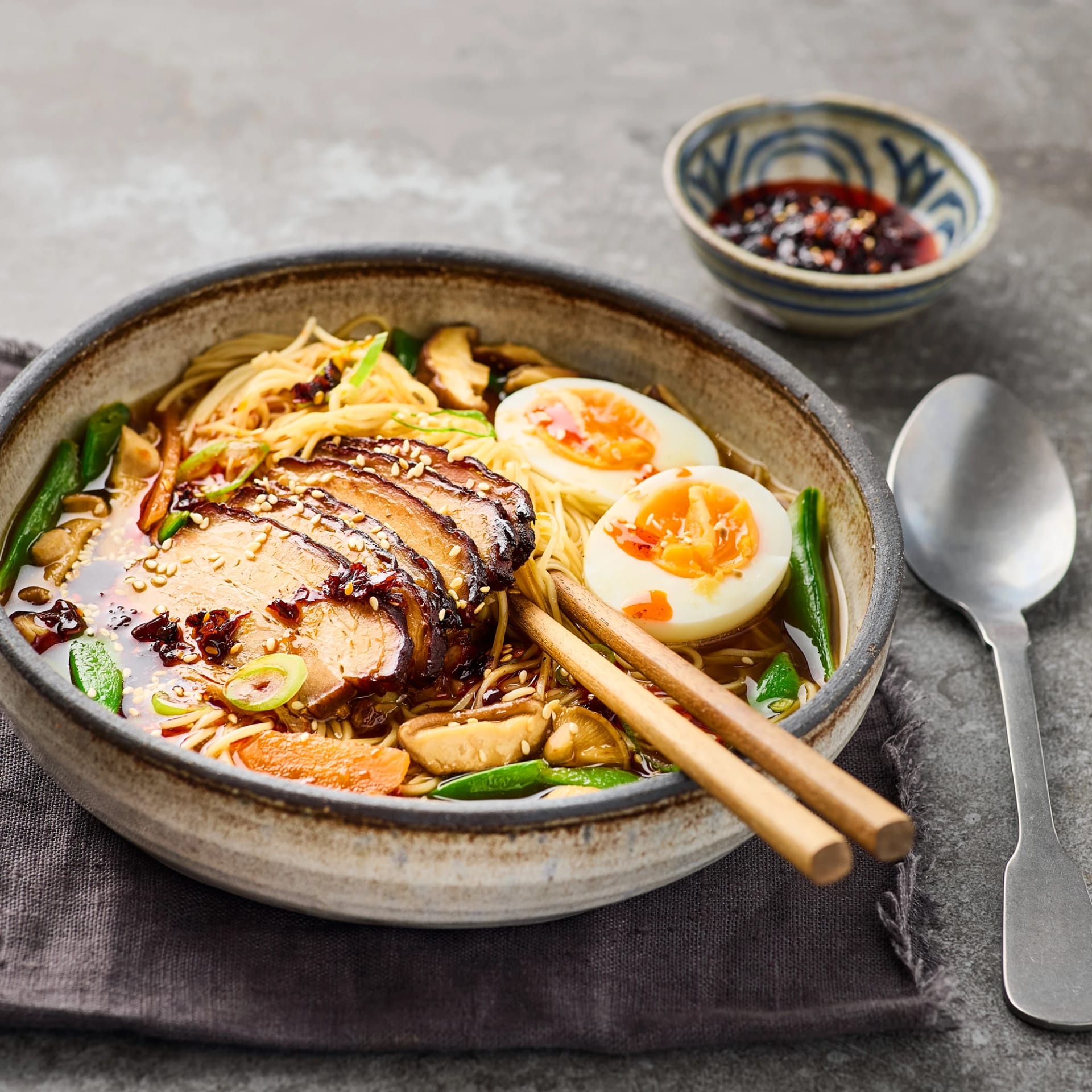 En djup skål med ramen, skivad fläsksvål halverat kokt ägg i en buljong toppad med chiliolja och sesamfrön.