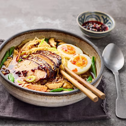 En djup skål med ramen, skivad fläsksvål halverat kokt ägg i en buljong toppad med chiliolja och sesamfrön.