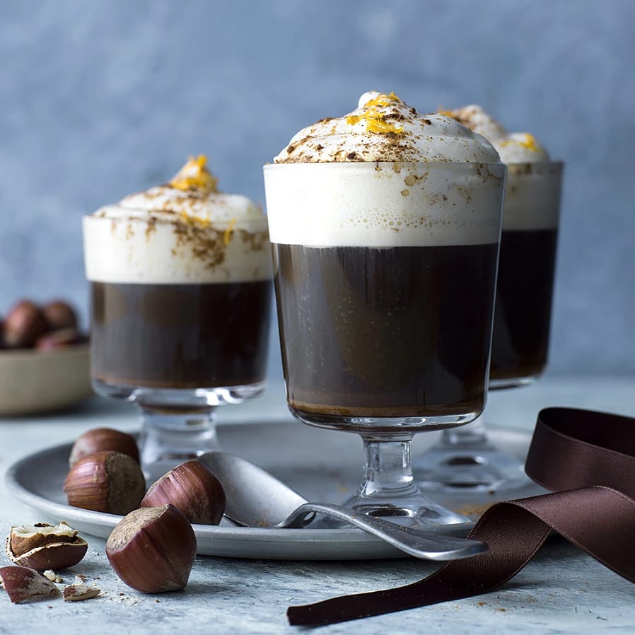 Glas på fot med en kaffedrink toppad med grädde och apelsinskal.