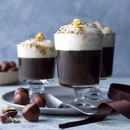 Glas på fot med en kaffedrink toppad med grädde och apelsinskal.
