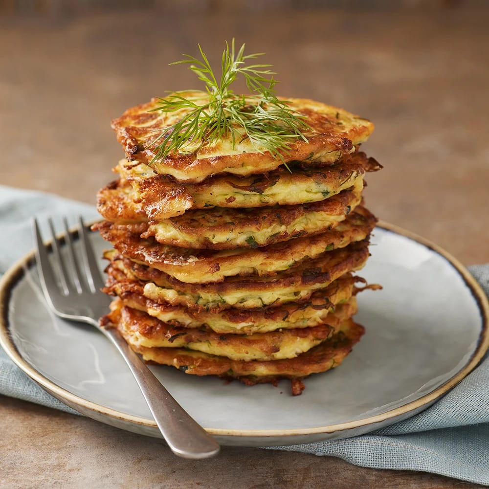En stapel zucchiniplättar med fetaost och dill på en tallrik, toppad med dill och en gaffel bredvid.