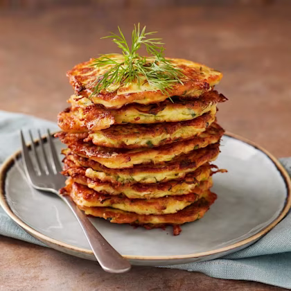En stapel zucchiniplättar med fetaost och dill på en tallrik, toppad med dill och en gaffel bredvid.