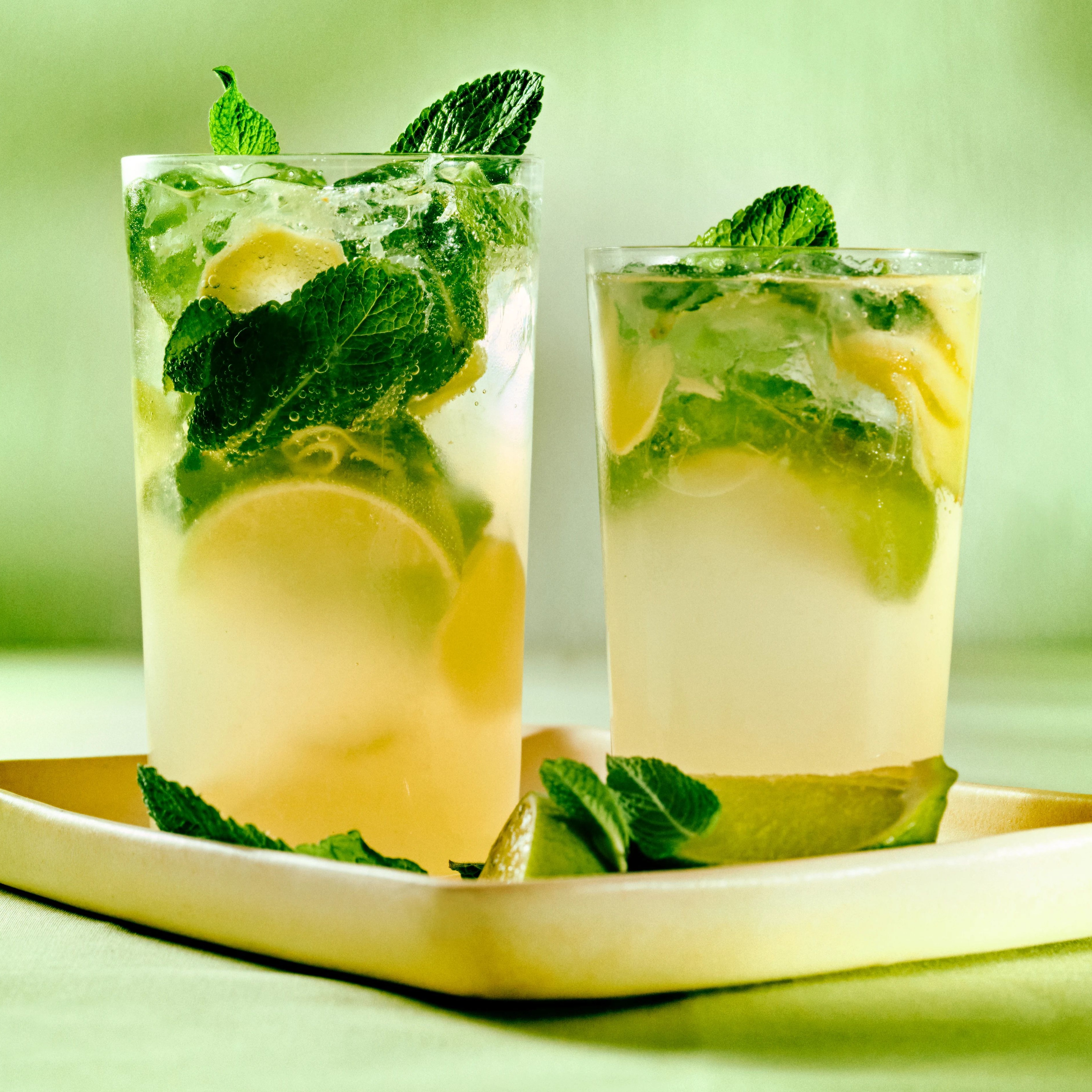 Två drinkar med lime och mynta på en vit bricka mot grön bakgrund.