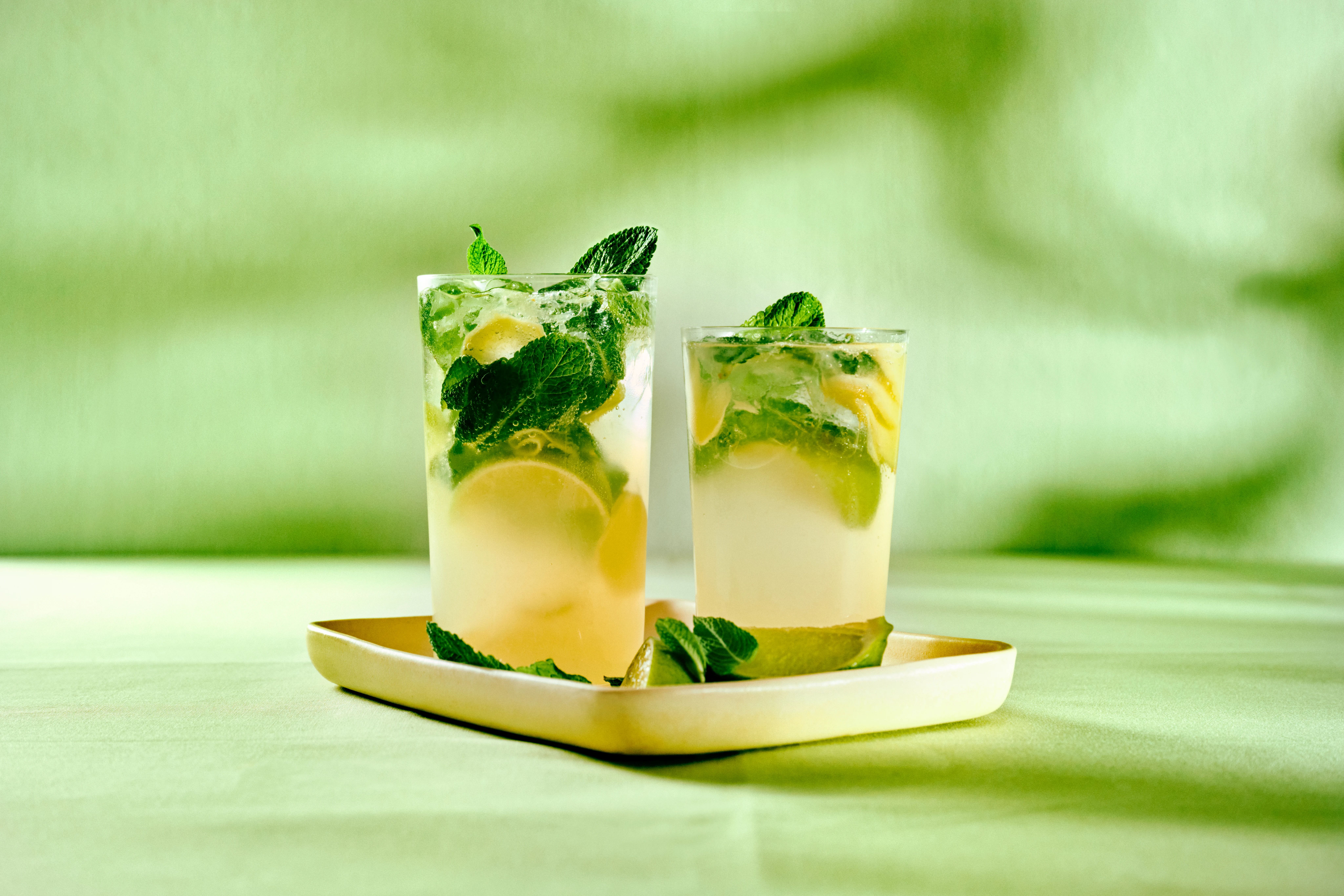Två drinkar med lime och mynta på en vit bricka mot grön bakgrund.