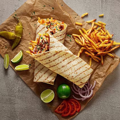 Två wraps med pommes frites och grönsaker, omgivna av limeklyftor, jalapeños, tomatskivor och lök på papper.