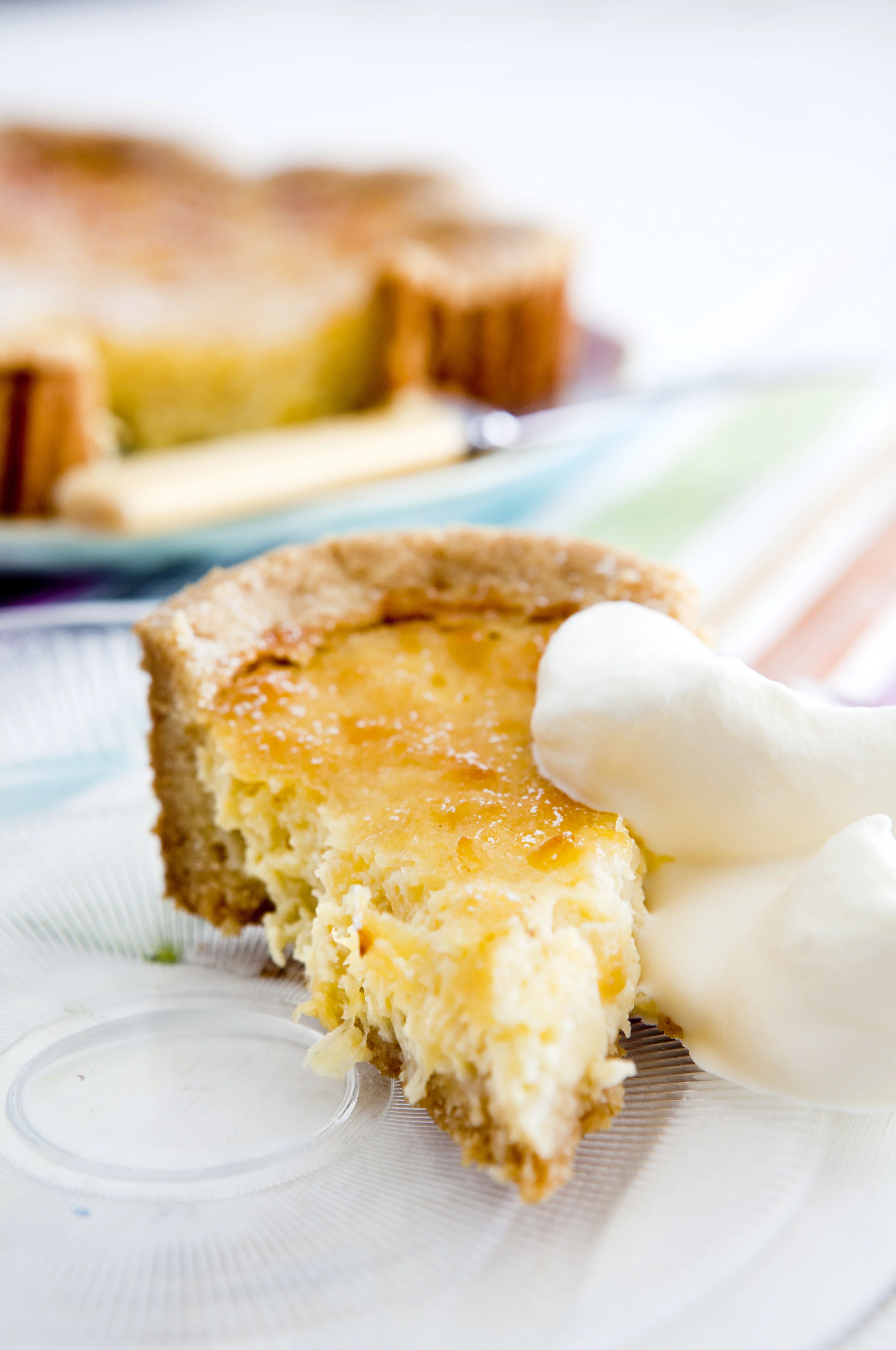 En bit ananaspaj med en klick vispad grädde på en tallrik, resten av pajen syns i bakgrunden.
