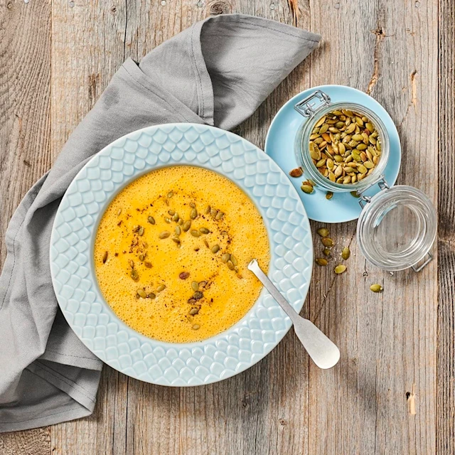 Pumpasoppa toppad med pumpakärnor och kryddor i en djup tallrik, med en sked och en burk pumpakärnor bredvid