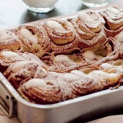 Kanelbullar med glasyr, täckta av florsocker, i en metallform.