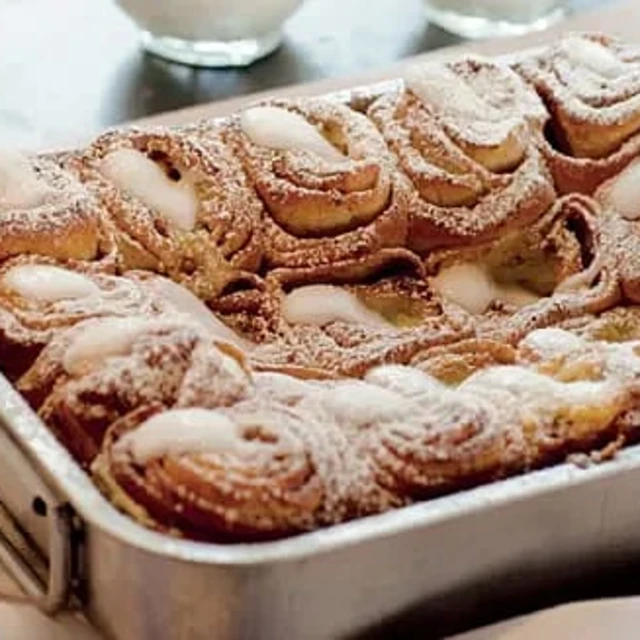 Kanelbullar med glasyr, täckta av florsocker, i en metallform.