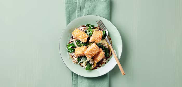 Panerad tofu med ris spenat och lök på en tallrik med gaffel.