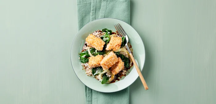 Panerad tofu med ris spenat och lök på en tallrik med gaffel.