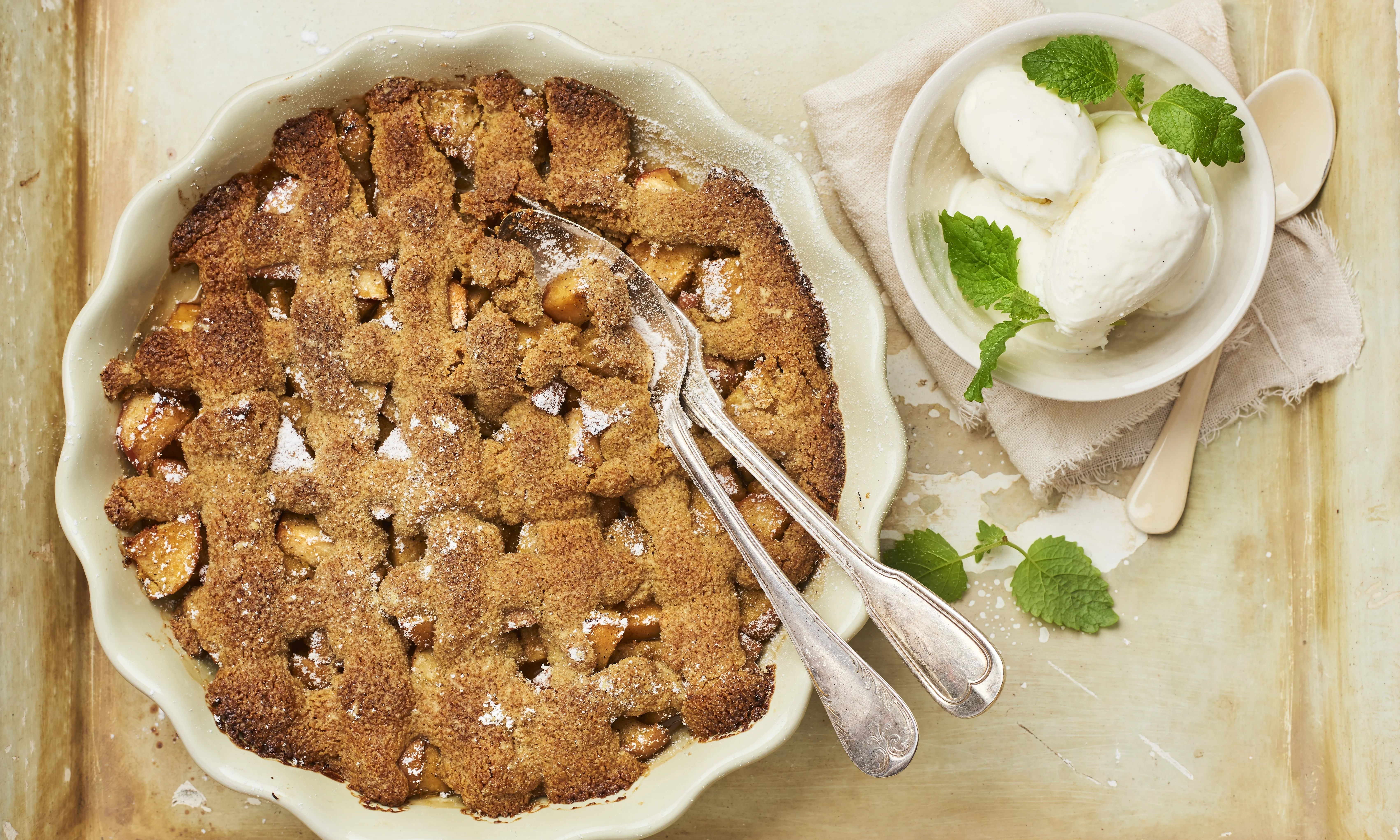 Äppelpaj med kanel och socker, serverad med vaniljglass och mynta. Två skedar ligger på pajen.
