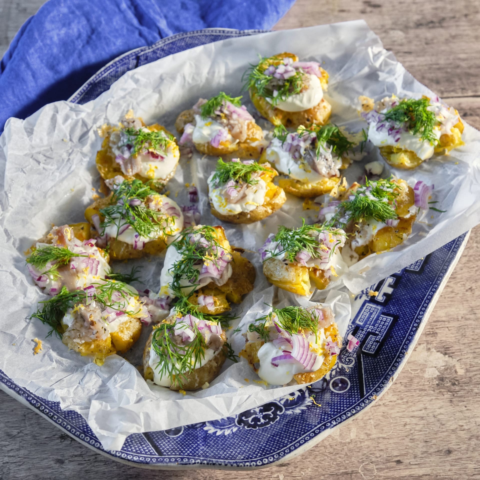 Krispig potatis toppad med brantevikssill, gräddfil, rödlök och dill på ett fat med bakplåtspapper