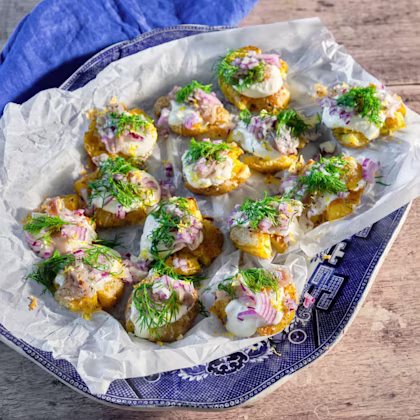 Krispig potatis toppad med brantevikssill, gräddfil, rödlök och dill på ett fat med bakplåtspapper