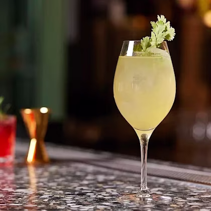 Gul drink i vinglas med is och koriander som garnering stående på marmorbord i bar.