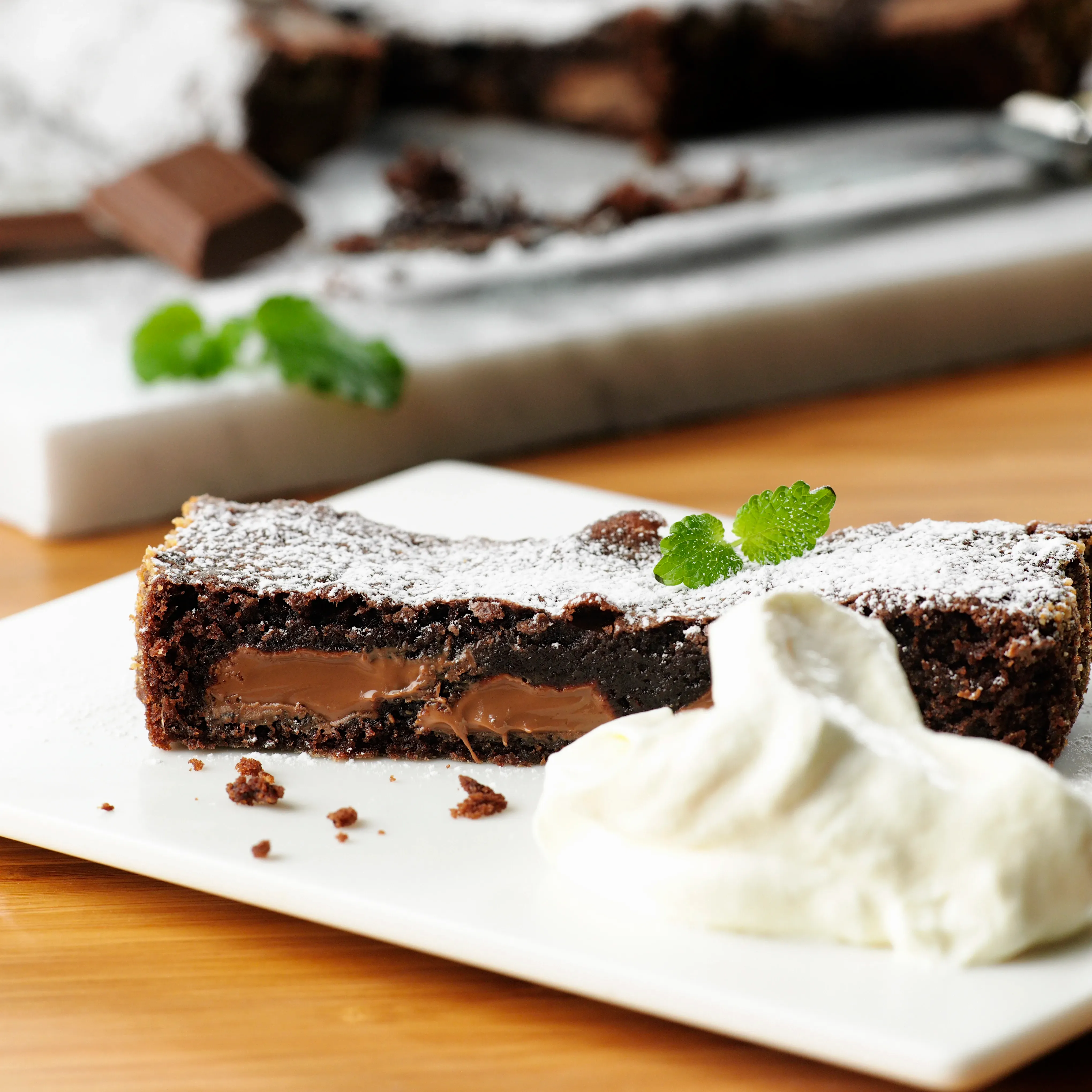 En vit fyrkantig tallrik med en saftig bit kladdkaka. Serverad med mynta och en klick grädde. 