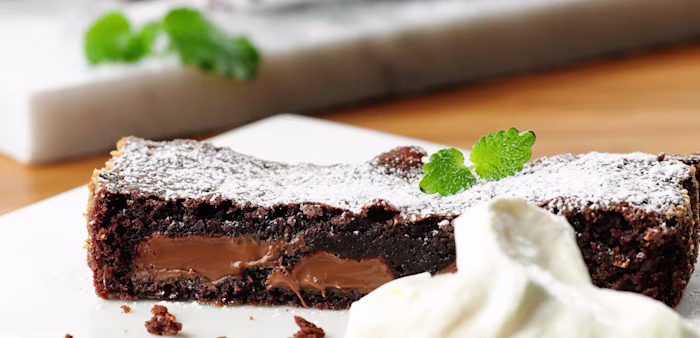 En vit fyrkantig tallrik med en saftig bit kladdkaka. Serverad med mynta och en klick grädde.