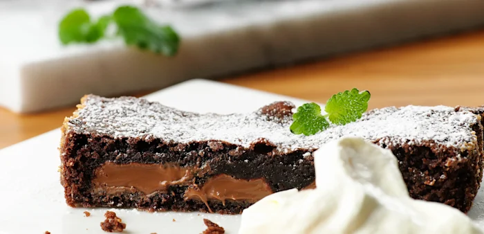 En vit fyrkantig tallrik med en saftig bit kladdkaka. Serverad med mynta och en klick grädde.