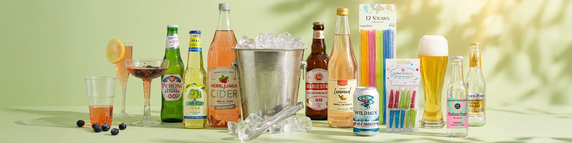Dryckesbord med glas, drinkar och flaskor samt is i hink, med texten “Peroni 0.0”, “Somersby”, “Herrljunga Cider Smultron”, “Mariestad Alkoholfri”, “Wild Mix”, “12 Straws”, “Cocktail Picks” och “Fever-Tree Tonic”. Klicka för att handla.