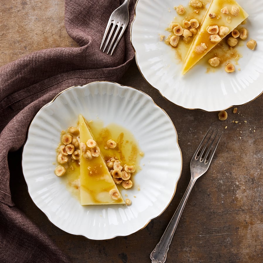 Vit talrik med vågiga kanter. En bit hårdost täckt med brynt smör och hasselnötter. 
