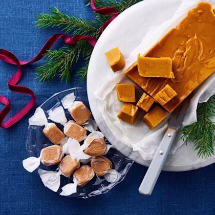 Saffransfudge skuren i bitar på ett fat med kniv och granris, samt inslagen saffransfudge i papper på ett glasfat.