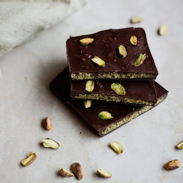 Tre bitar Dubaichoklad med pistagenötter på marmoryta, pistagenötter utspridda runtomkring.