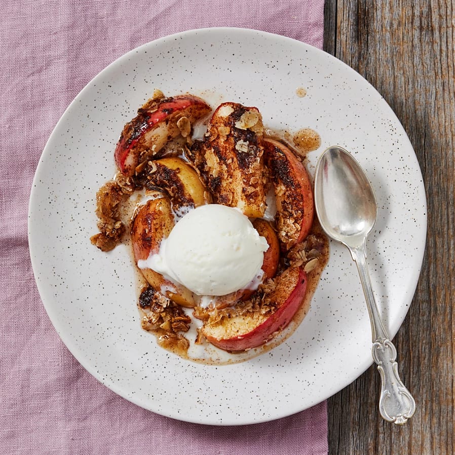 Ugnsbakade äpplen med kanel och havregryn, toppade med en kula vaniljglass, serverade på en vit tallrik.