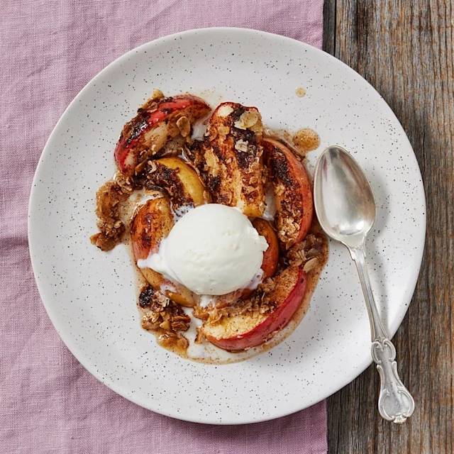 Ugnsbakade äpplen med kanel och havregryn, toppade med en kula vaniljglass, serverade på en vit tallrik.