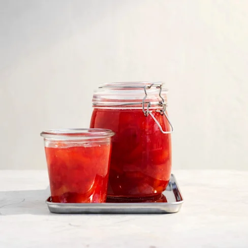 Två burkar med plommonmarmelad i glas, en stor och en liten, på en metallbricka mot en ljus bakgrund.