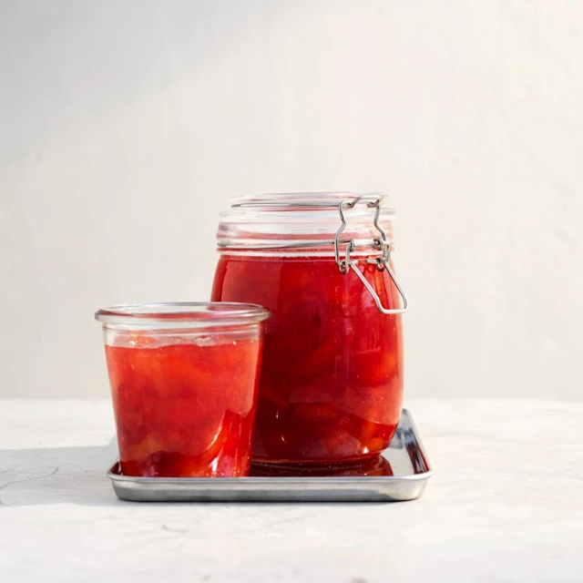 Två burkar med plommonmarmelad i glas, en stor och en liten, på en metallbricka mot en ljus bakgrund.