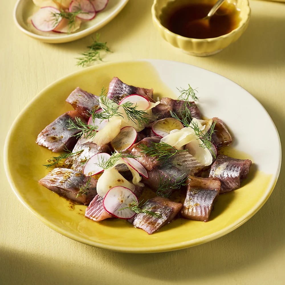 Matjesill med brynt sojasmör, toppad med gari (inlagd ingefära), rädisor och dill på en tallri.