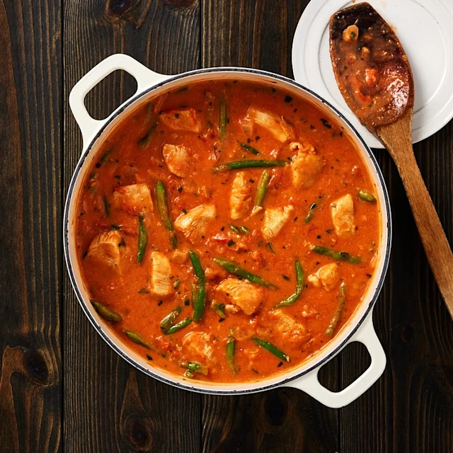 En stor gryta med röd sås, bitar av kyckling och gröna bönor.