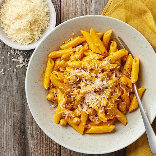 Pasta med sås och riven ost i en skål, serverad med en gaffel och en gul servett. Riven ost i en skål bredvid.