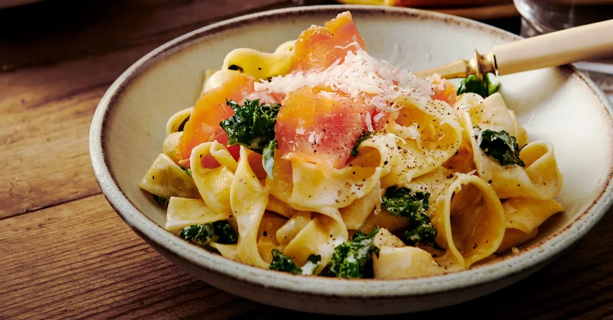 Pasta med grönkål och rökt lax, toppad med riven ost, serverad i en skål på ett träbord.