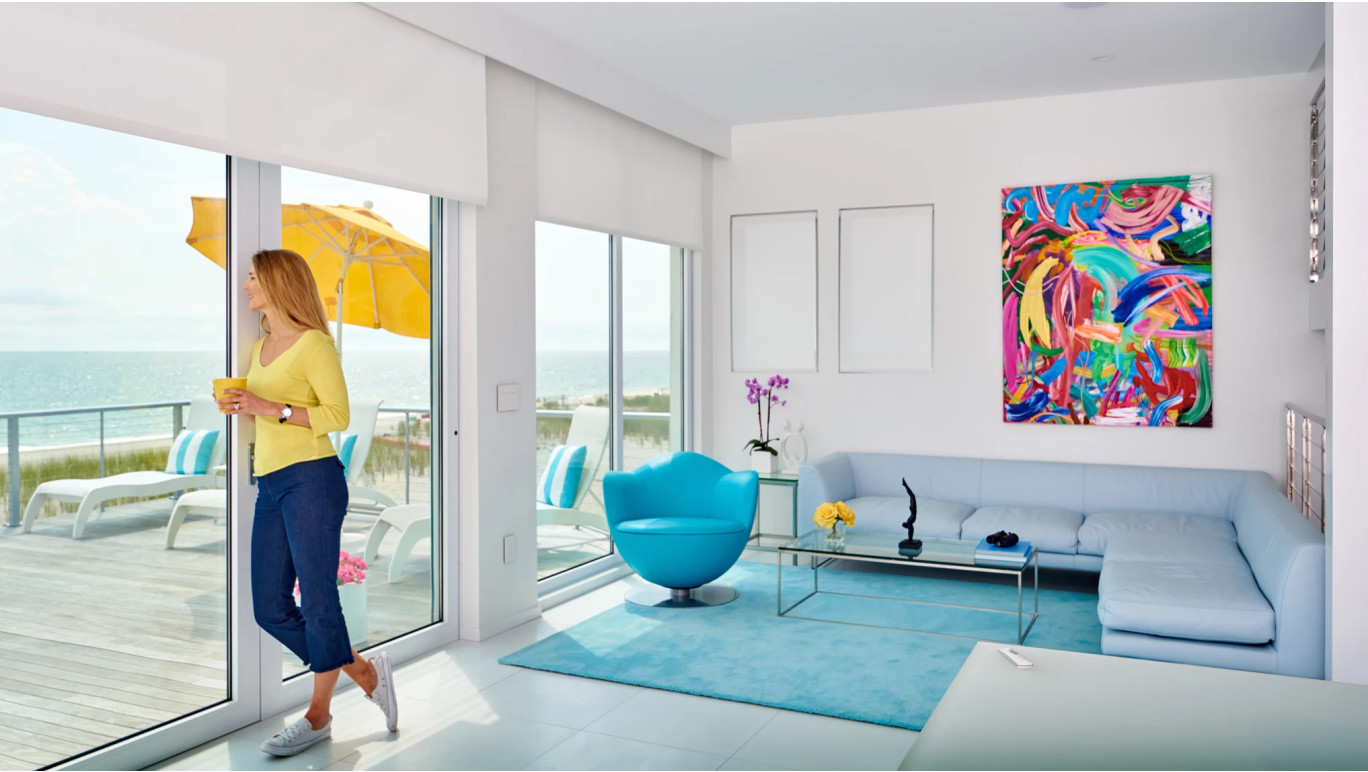 Woman standing looking out the window in a living room with Somfy Automation Roller Shades