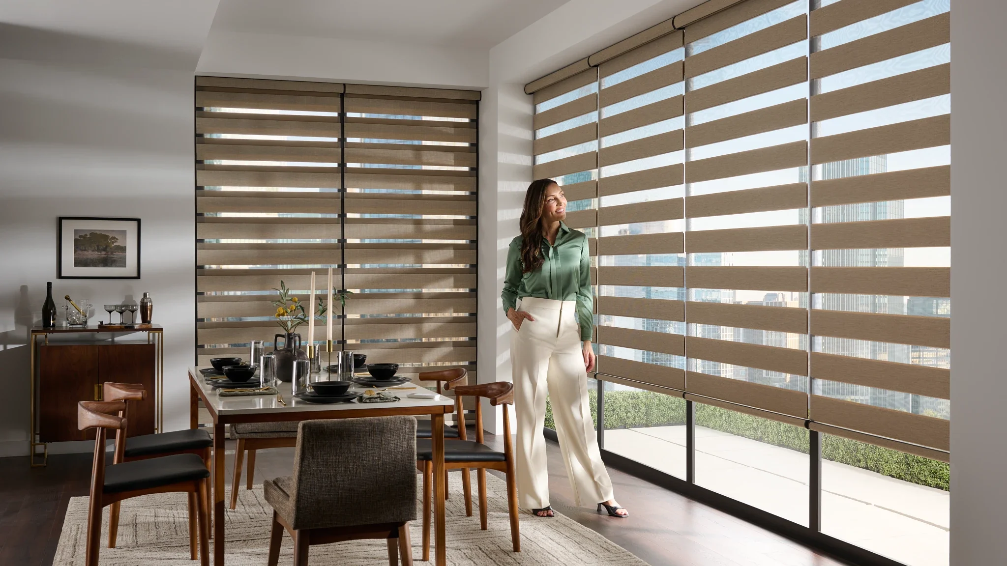 Woman standing in in a dining room, surrounded by banded shade window coverings.